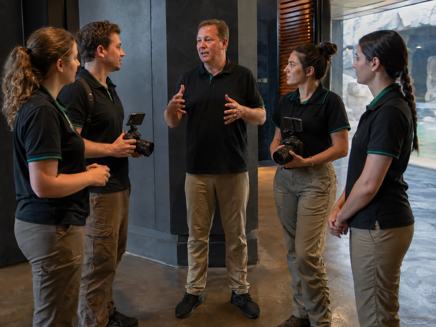 A venue manager briefing four uniformed photographers holding cameras before a shift.